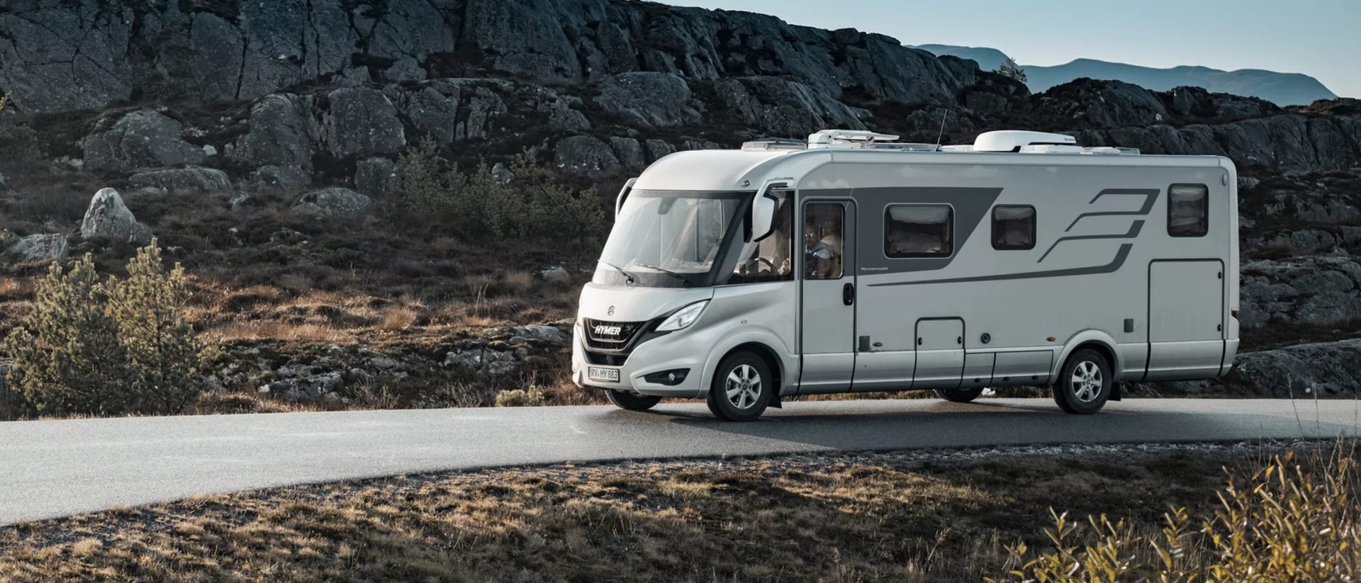 Een camper rijdt langs een fjord, de rotsen in gouden avondlicht